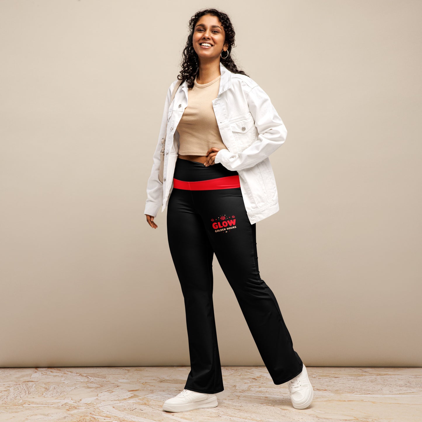 A woman is standing, wearing black flare leggings with a red waistband and 'GLOW Golden Hours' text on the front. She has her hands on her hips, smiling at the camera.
